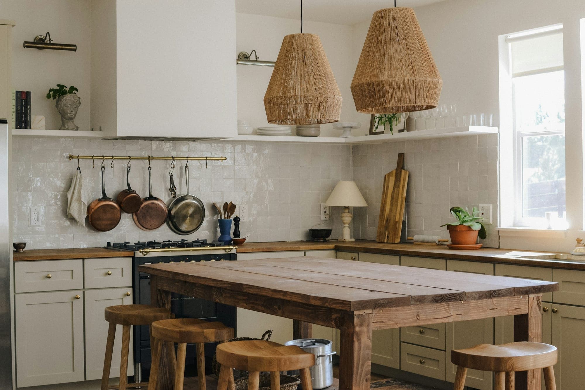 A warm kitchen with copper pans, woven pendant lamps and a wooden island
